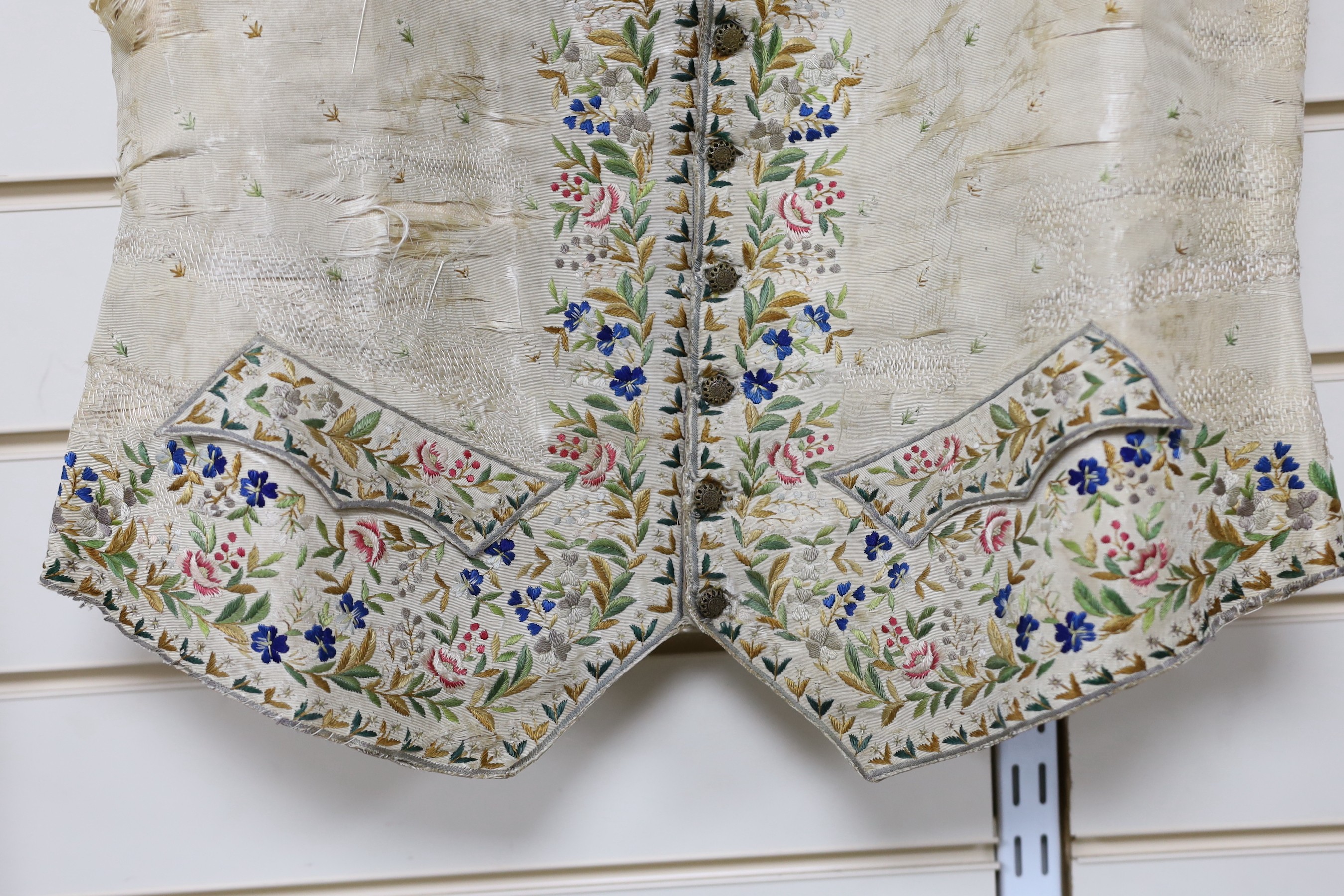 A late 18th early 19th century gentleman’s cream silk waistcoat Embroidered with polychrome silks in a floral design. (The main body of the waistcoat darned and damaged, but the embroidered sections complete).